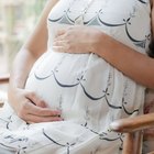 Beautiful pregnant woman sitting at bed and holds hands on belly in bedroom at home.
