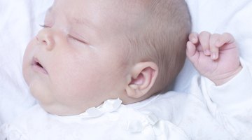 Baby smiling in bed with eyes closed and arms out.