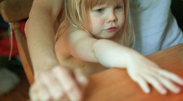 Pregnant woman holding crying girl while talking on telephone