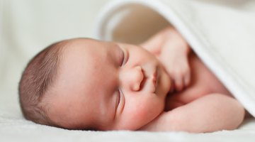 Baby smiling in bed with eyes closed and arms out.