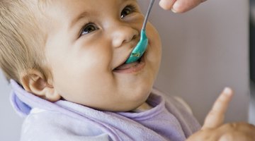 White dish of apple sauce with blue baby spoon.