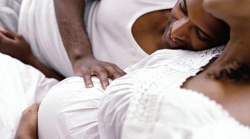 Beautiful pregnant woman sitting at bed and holds hands on belly in bedroom at home.