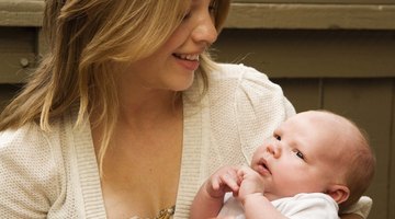 Beautiful pregnant woman sitting at bed and holds hands on belly in bedroom at home.