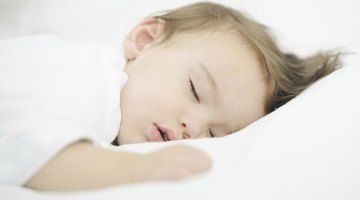 Baby smiling in bed with eyes closed and arms out.