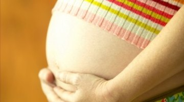 Pregnant woman lying on bed with her hand at belly